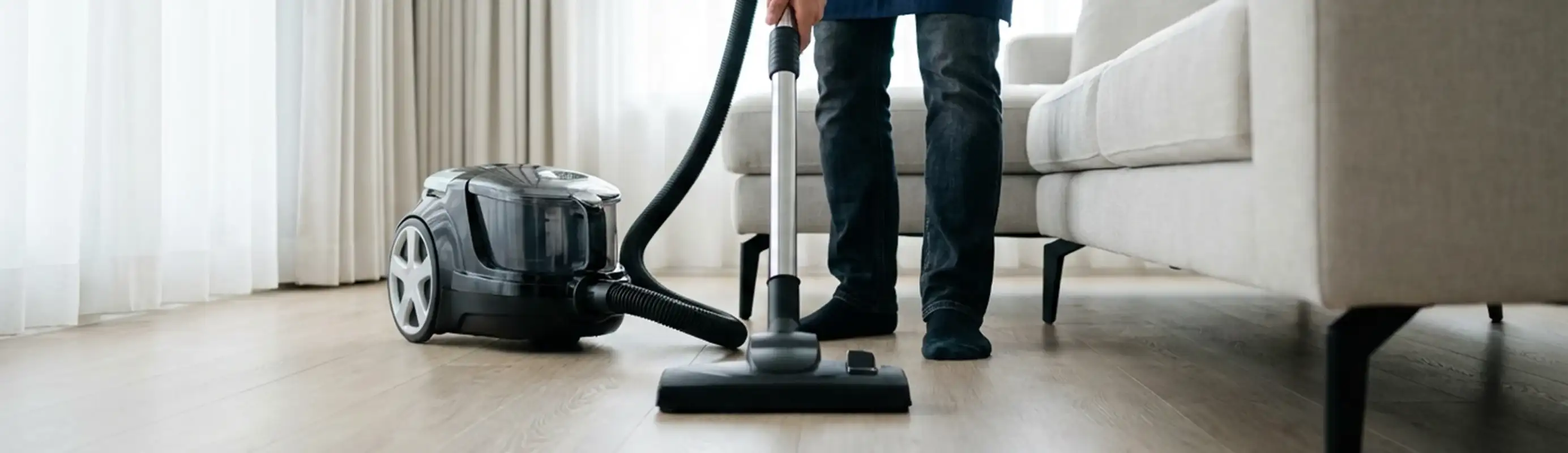 Professional house cleaner vacuuming a living room floor with a canister vacuum cleaner, Fort Collins, CO.