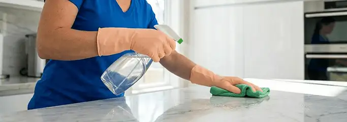 Maid service worker spraying and wiping a kitchen countertop with a microfiber cloth for sanitizing, Fort Collins, CO.