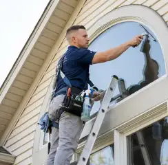 Professional window cleaner on a ladder using a squeegee to clean an exterior arched window, Fort Collins, CO.