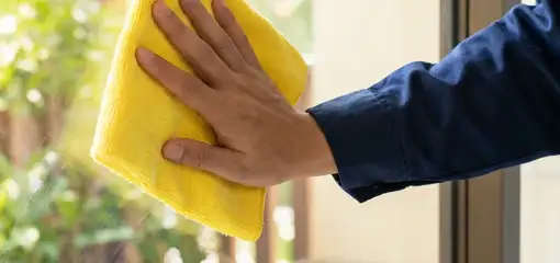 House cleaner wiping a glass window with a yellow microfiber cloth for streak-free cleaning, Fort Collins, CO.